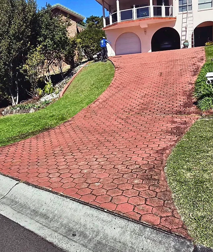 A faded red stamped-concrete driveway, stained and patchy, while the crew washes it before painting