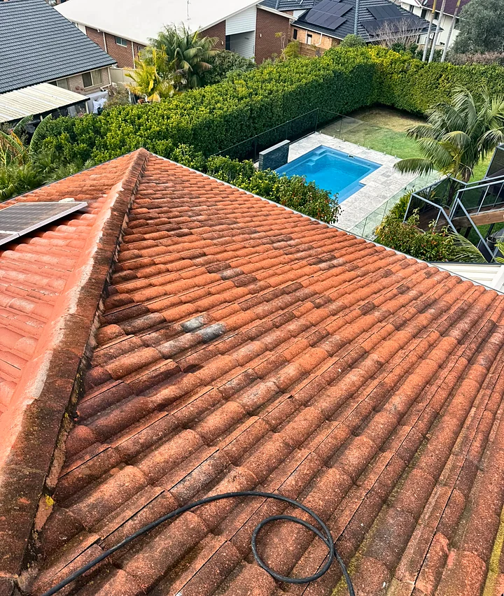 A terracotta tiled roof, weathered and patchy with moss along the ridge, before painting